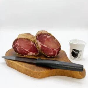Tranche de Coppa de l’île de Beauté posée sur une planche avec couteau et gobelet corse