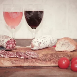 Saucisson sec au sanglier tranché sur planche en bois avec tomates, pain et vin rouge – charcuterie Montserret